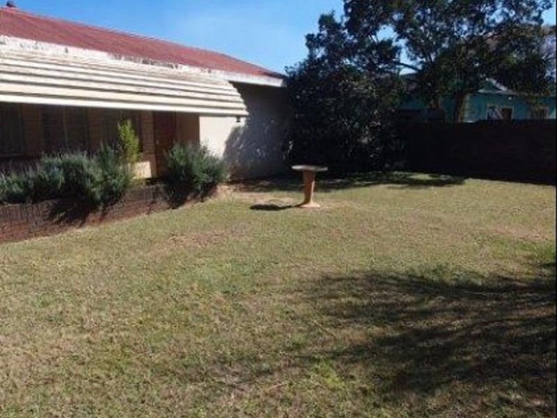 A rear garden area featuring a lawn, a brick boundary wall, and a metal window awning attached to the house exterior.