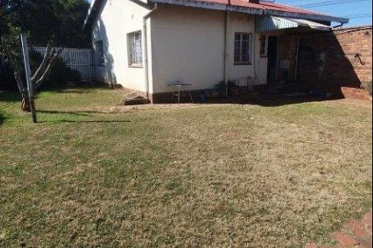 Rear view of the property featuring a brick chimney, corrugated metal roof, and a spacious backyard with a brick paved pathway.