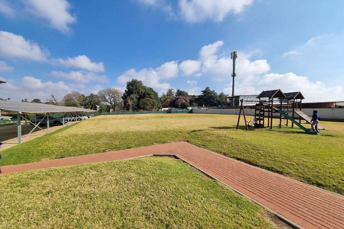 Spacious communal garden area featuring a paved walkway, solar carport structure, and playground equipment within a secure perimeter.
