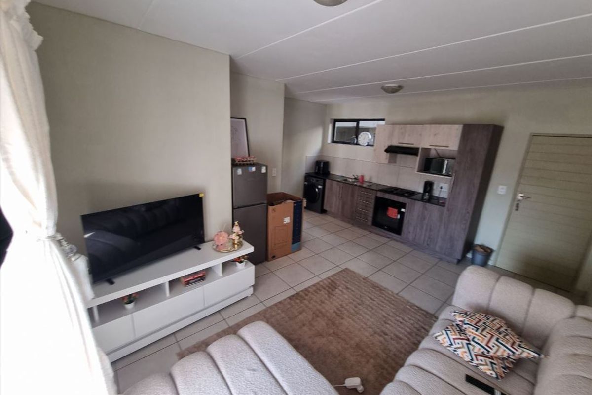 Open-plan living area featuring a compact kitchen with built-in cabinetry, oven, and hob, seamlessly connected to the lounge space with tiled flooring throughout.
