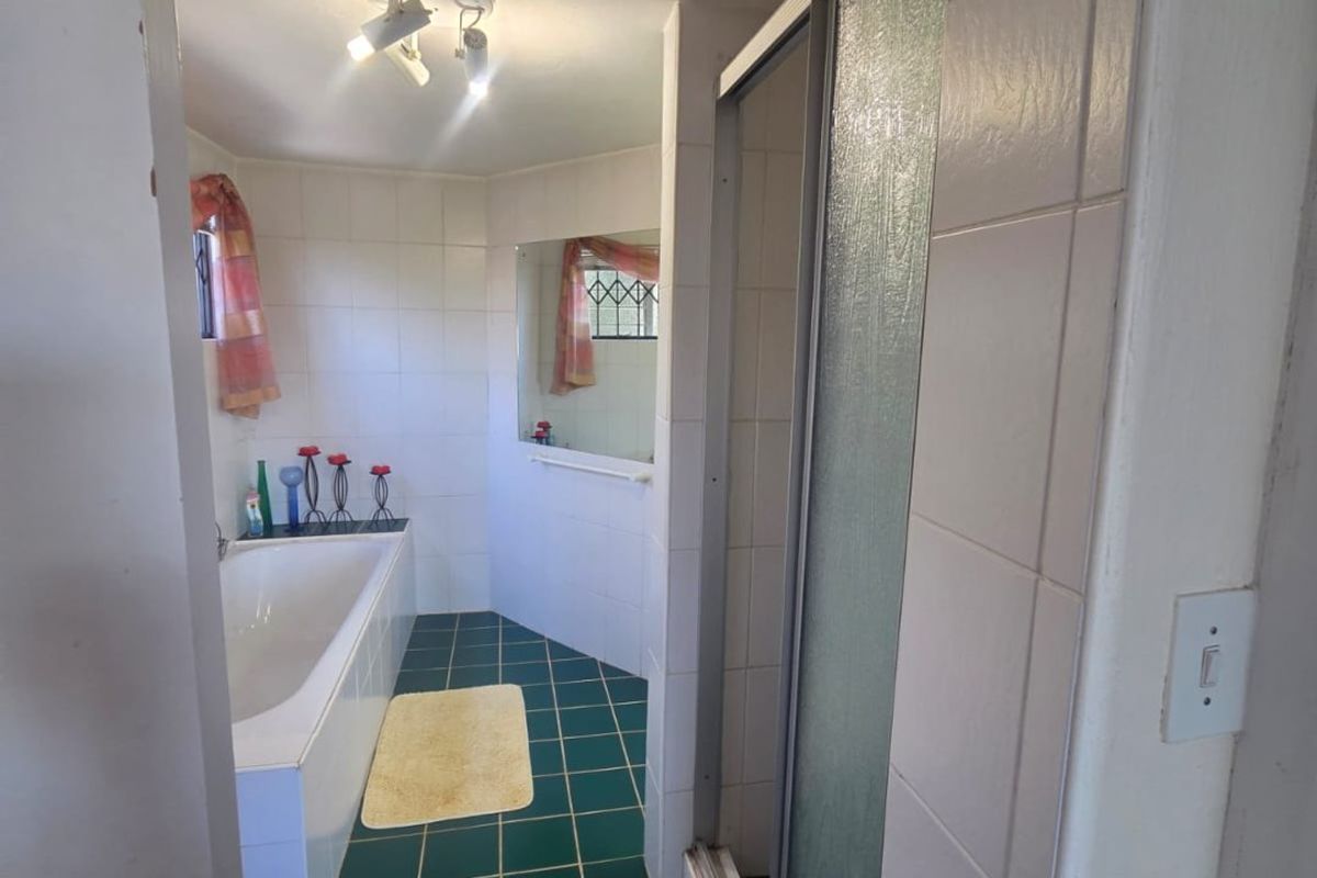 A functional bathroom featuring a built-in bathtub, separate shower enclosure, and tiled finishes, offering a classic layout with potential for modern updates.