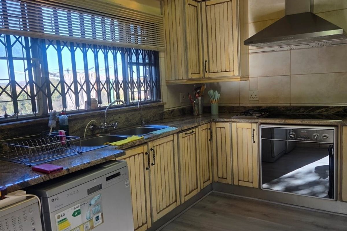 A functional kitchen featuring granite countertops, built-in oven, stainless steel extractor fan, and fitted cabinetry with a classic finish.