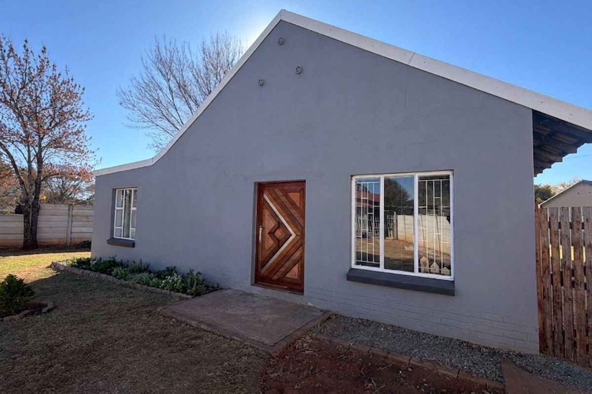 A well-maintained rear exterior view of the house featuring a modern timber entrance door, security-fitted windows, and a private garden area.