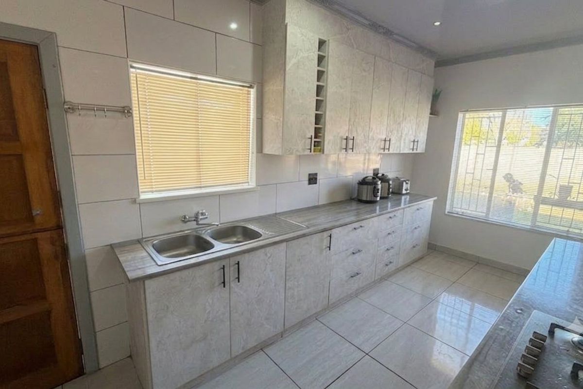 A functional kitchen featuring light-toned cabinetry, laminate countertops, a double stainless steel sink, and tiled finishes throughout.