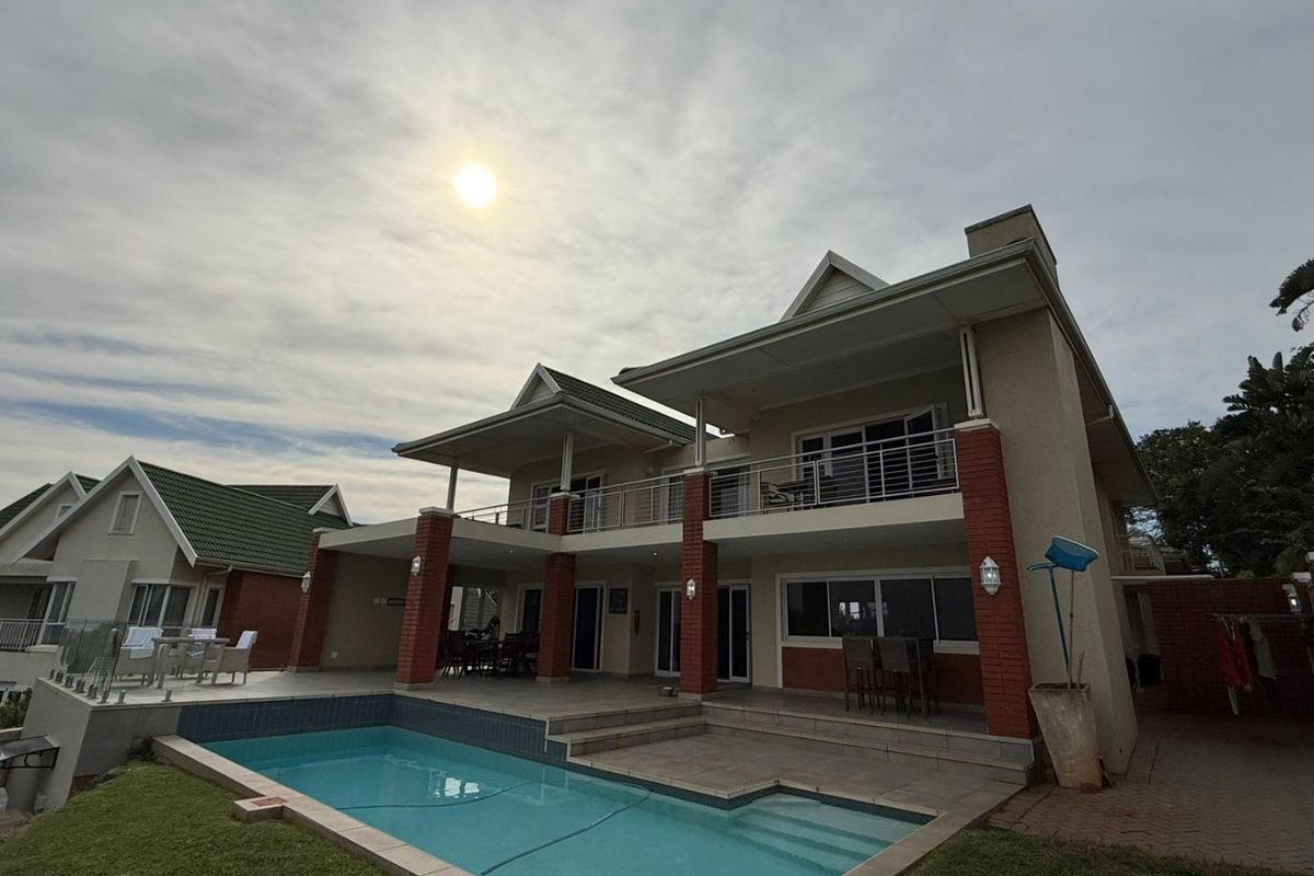 Rear elevation of a two-story house featuring a swimming pool, covered patio, and an upper-level balcony with metal railings.