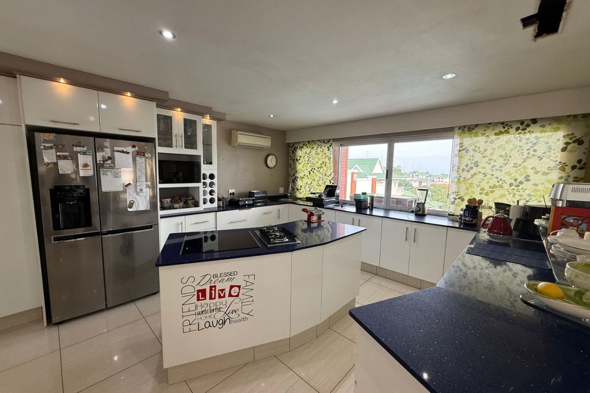 Modern kitchen featuring white cabinetry, dark stone countertops, a central island with a built-in hob, and tiled flooring.