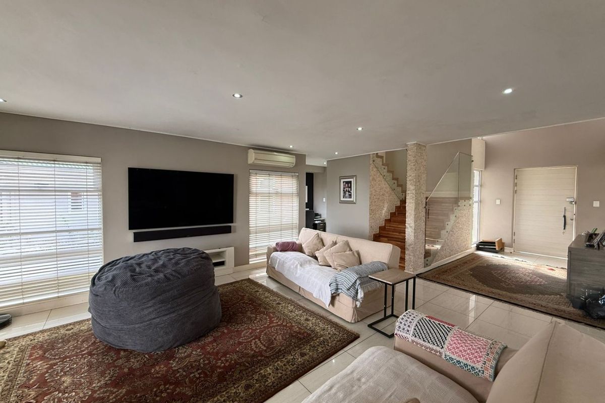 Spacious open-plan living area featuring polished tiled floors, recessed lighting, a modern glass staircase, and a stone-clad feature pillar.