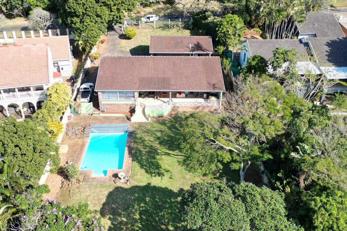 Aerial view of the property featuring a swimming pool, spacious garden, covered patio, and tiled roof structure.