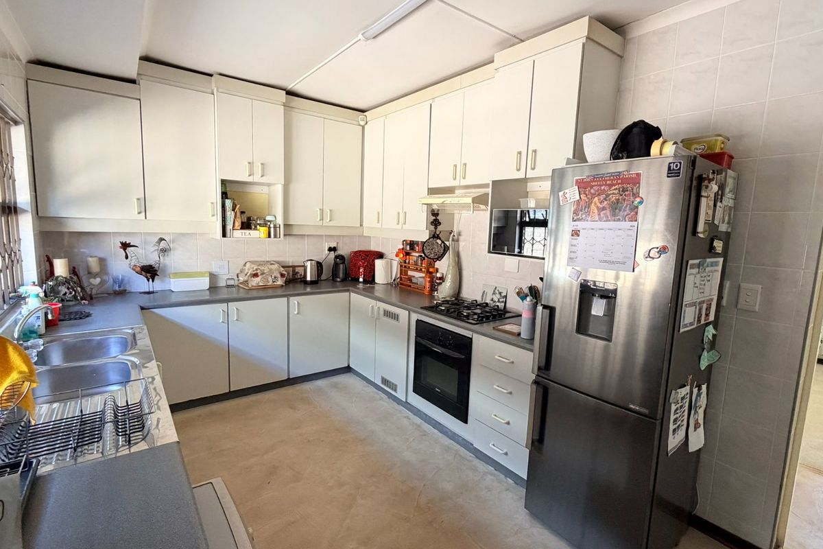 Functional kitchen featuring white built-in cabinetry, laminate countertops, a gas hob, built-in oven, and tiled splashbacks with security bars on the window.