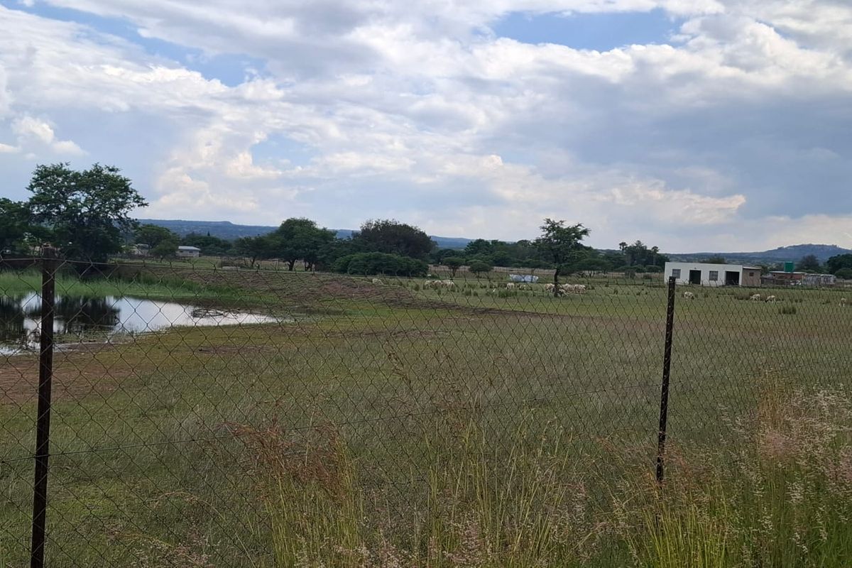 A wide-angle view of the farm landscape featuring open grazing land, a natural dam, and perimeter wire fencing.