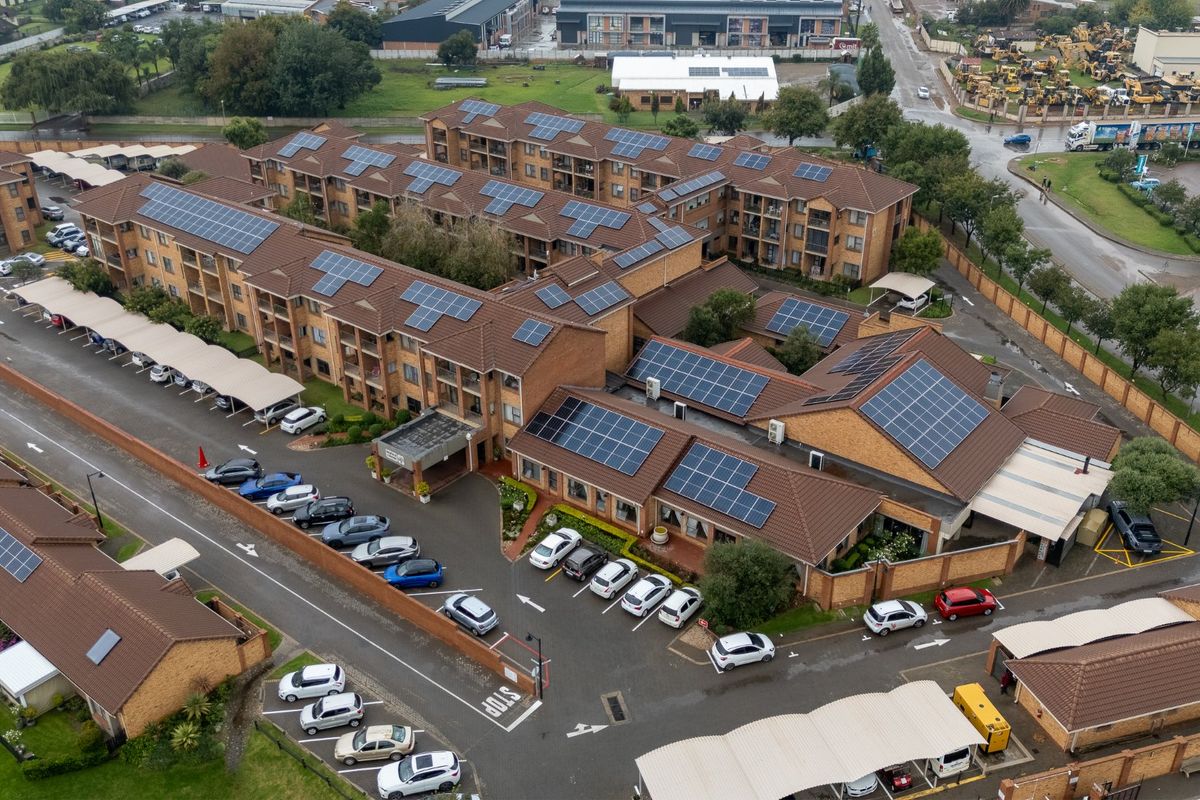 Aerial view of a multi-story apartment complex featuring extensive rooftop solar panel installations, covered parking bays, and paved access roads.