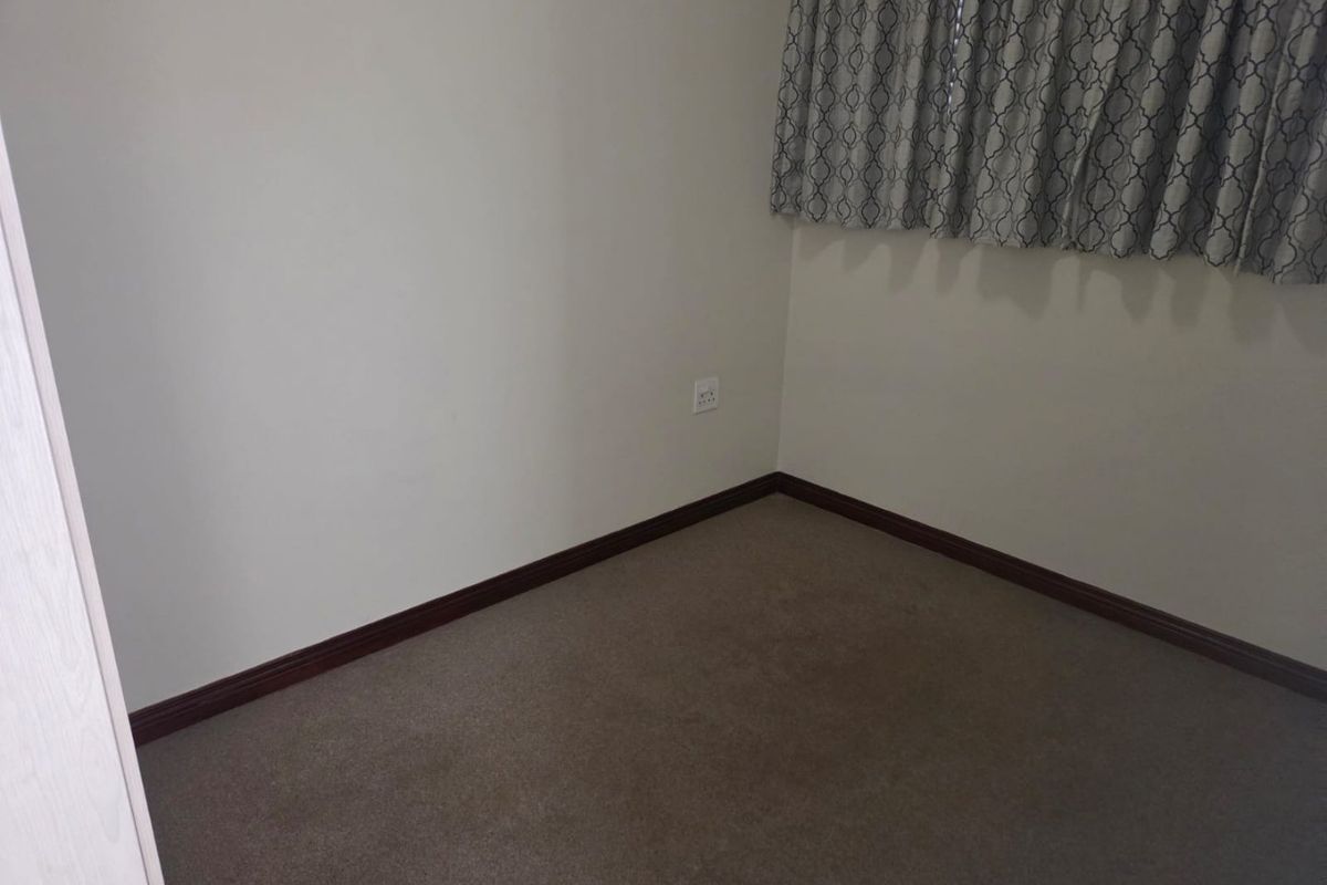 A clean, empty bedroom featuring neutral wall paint, carpeted flooring, and dark wood-tone skirting boards.
