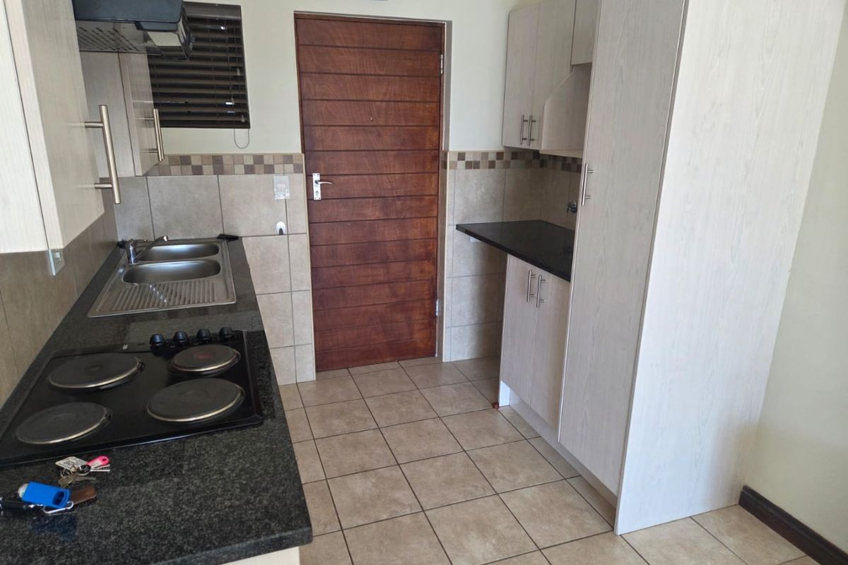 A functional kitchen featuring built-in cabinetry, granite countertops, an electric hob with extractor fan, and a double bowl sink with tiled finishes.