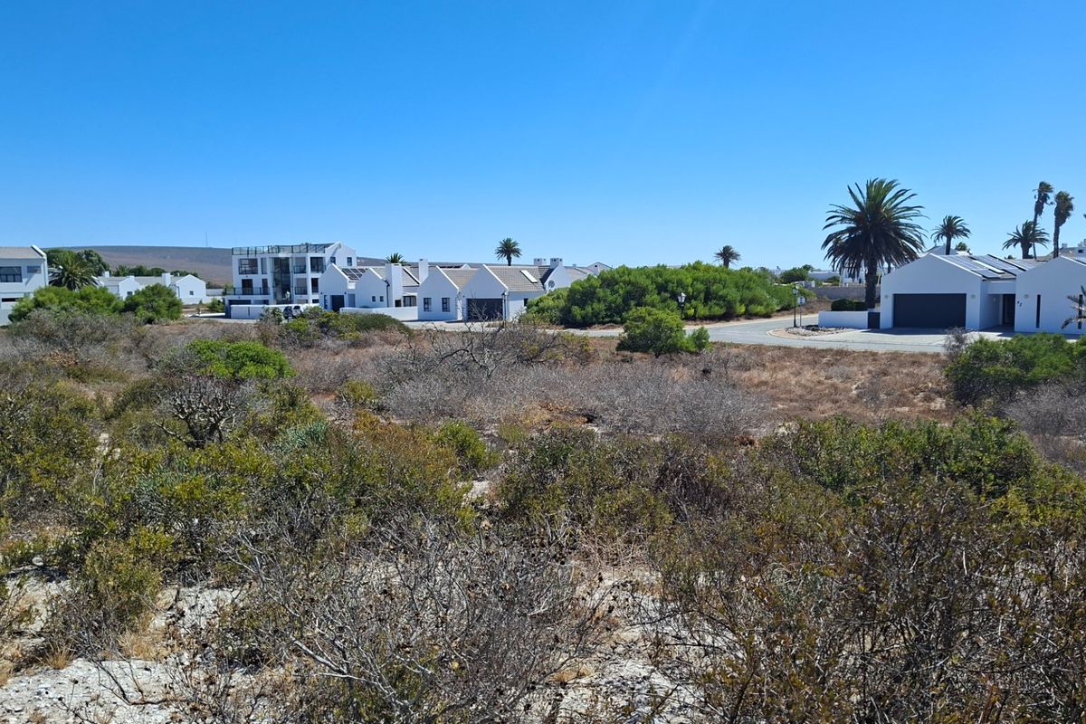 A view of a vacant residential plot featuring native coastal vegetation and sandy terrain, situated within a developed residential estate.