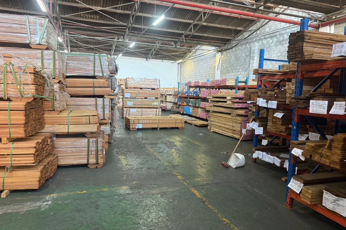 Industrial warehouse space featuring high ceilings with exposed steel trusses, fire sprinkler systems, concrete flooring, and extensive heavy-duty racking for storage.