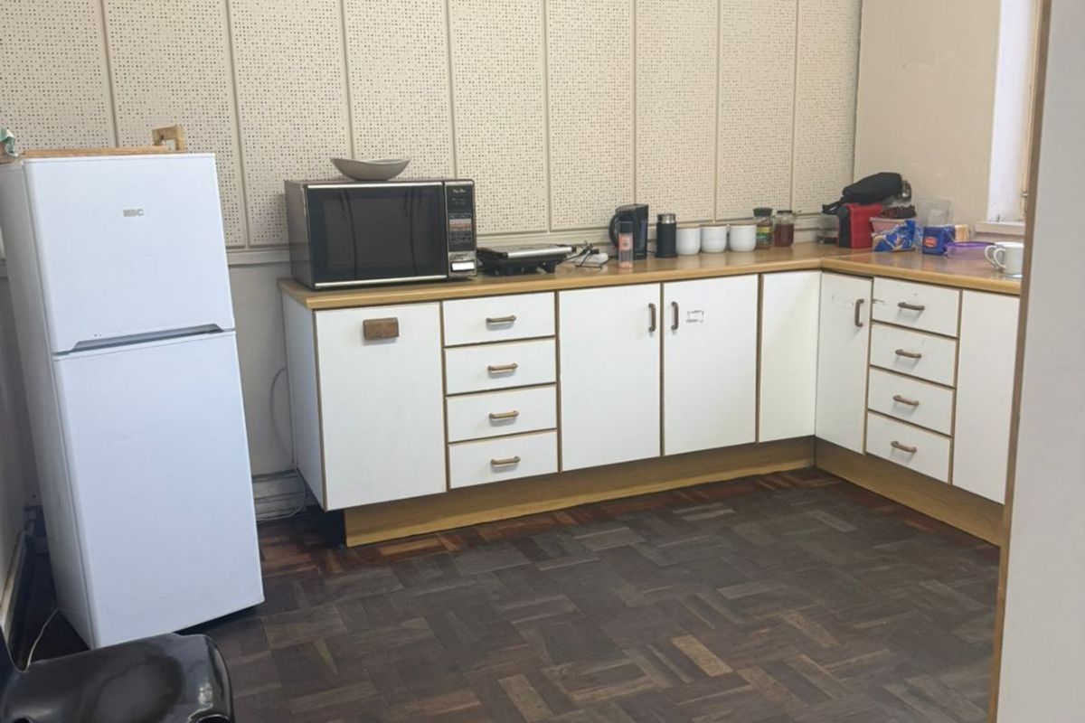 A functional kitchen area featuring white laminate cabinetry, wood-look parquet flooring, and distinctive acoustic wall paneling, offering a dated but practical industrial workspace.