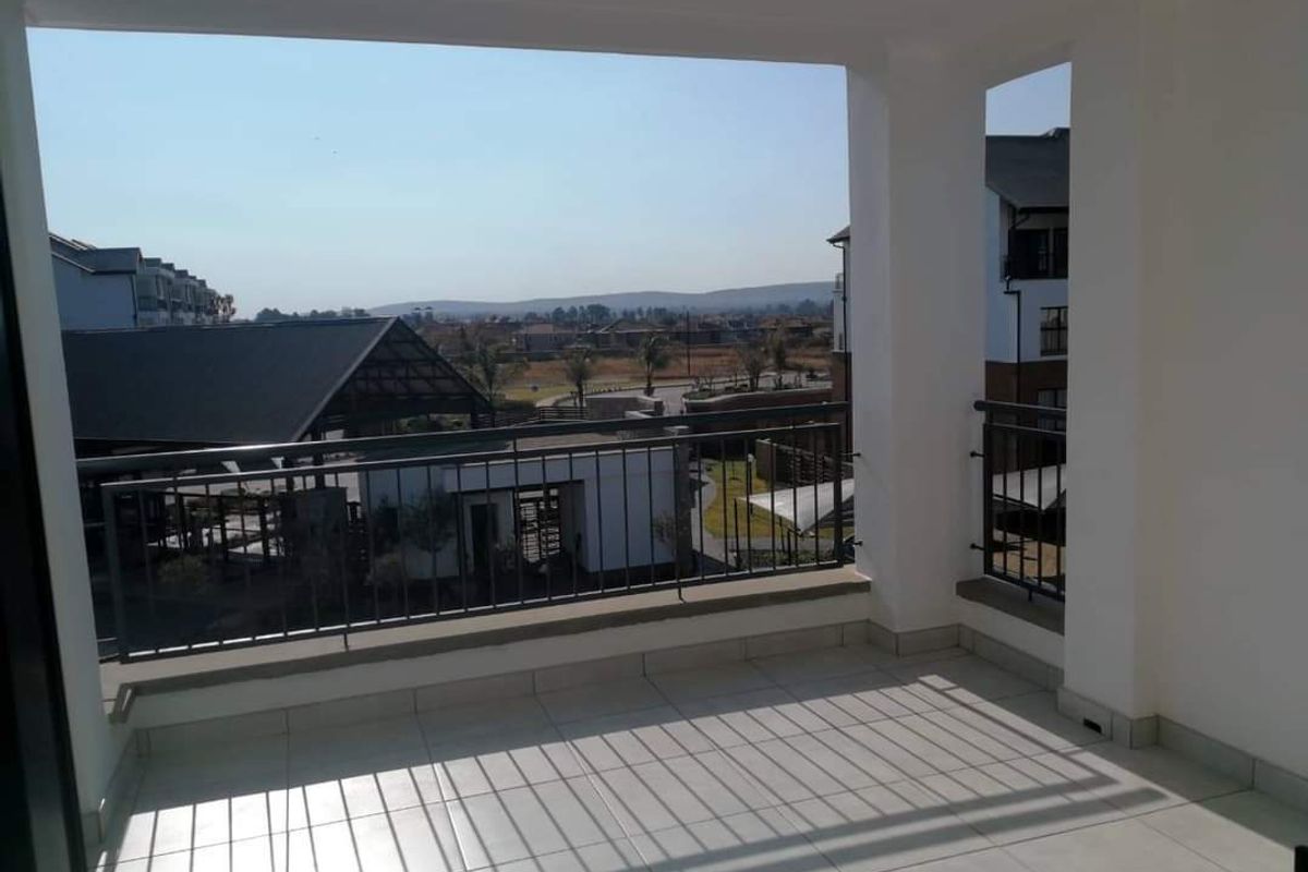 A spacious covered balcony featuring tiled flooring and a metal balustrade, offering clear views of the surrounding estate and landscape.
