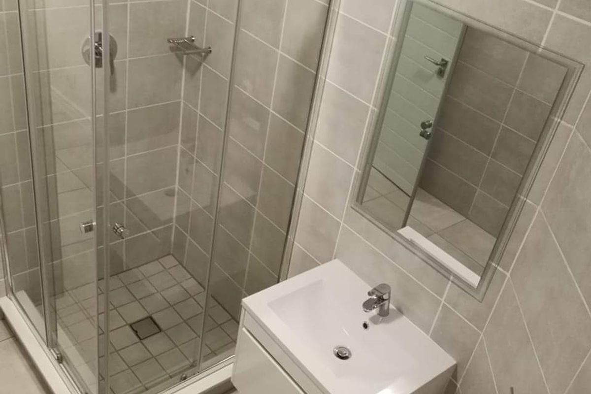 A modern, clean bathroom featuring a glass shower enclosure, a wall-mounted vanity with basin, and neutral floor-to-ceiling tiling.