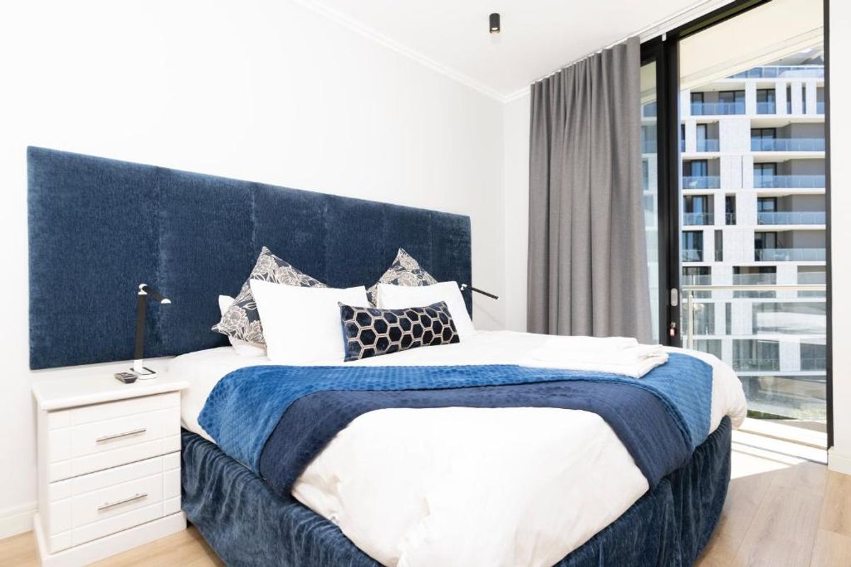 A well-maintained bedroom featuring laminate flooring and a large sliding glass door providing access to a balcony with urban views.