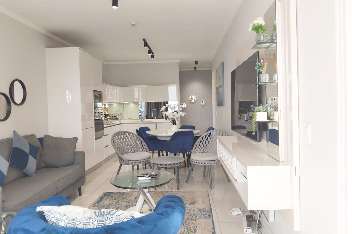 Modern open-plan living and kitchen area featuring sleek white cabinetry, integrated appliances, tiled flooring, and contemporary track lighting.