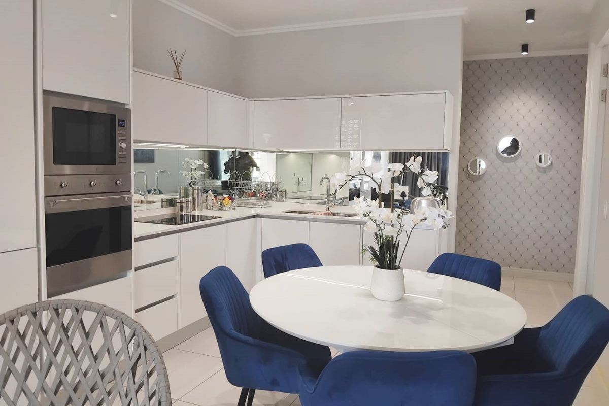 Modern open-plan kitchen featuring high-gloss white cabinetry, integrated appliances, a mirrored splashback, and sleek recessed ceiling lighting, seamlessly flowing into the dining area.