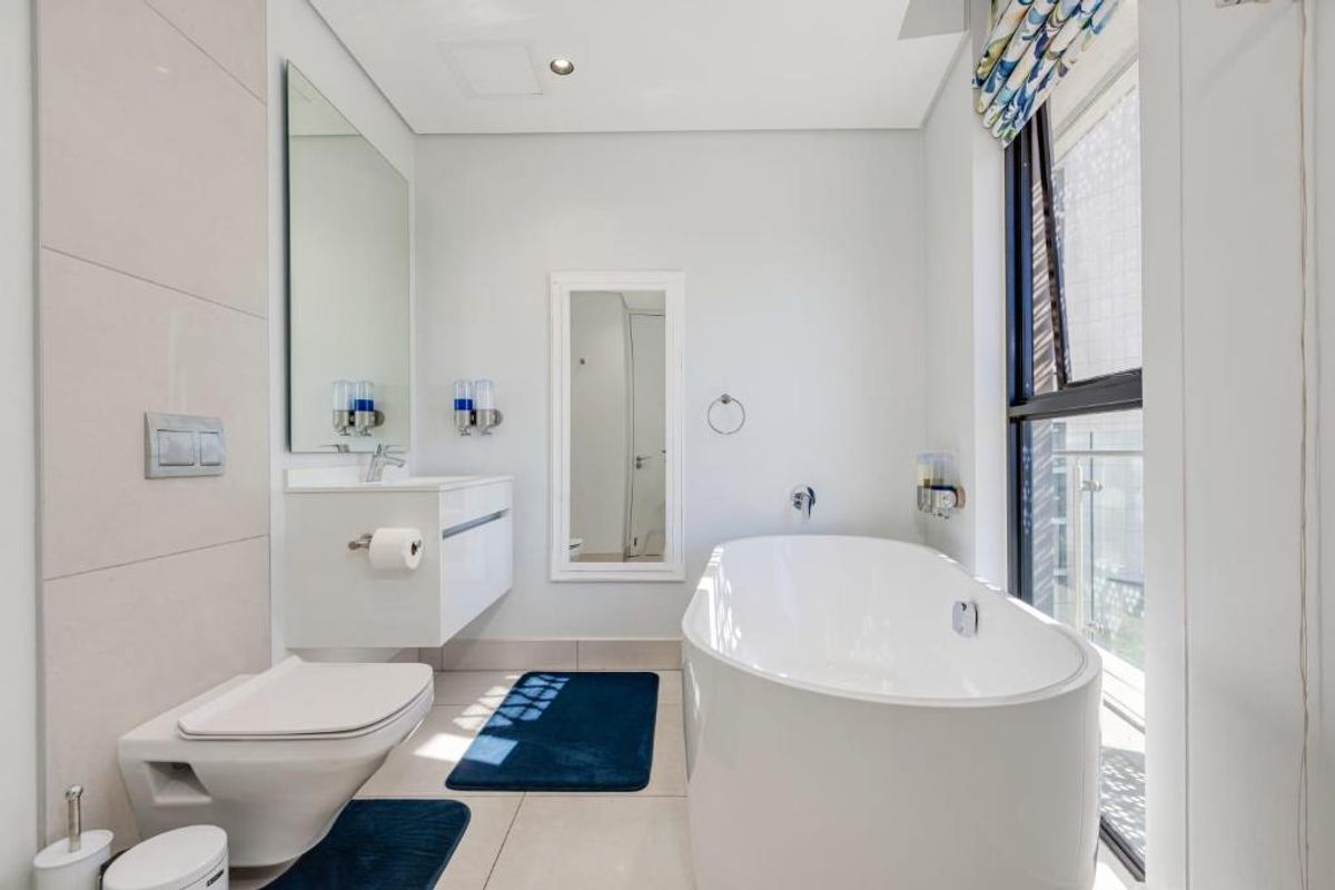 Modern bathroom featuring a wall-hung toilet with concealed cistern, a sleek wall-mounted vanity, and a contemporary freestanding bathtub next to a large window.