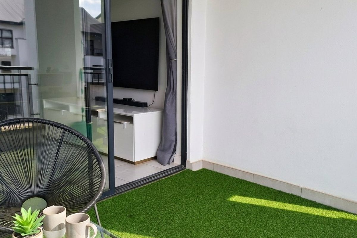 A compact balcony featuring artificial turf flooring and a large sliding glass door providing seamless access to the interior living space.