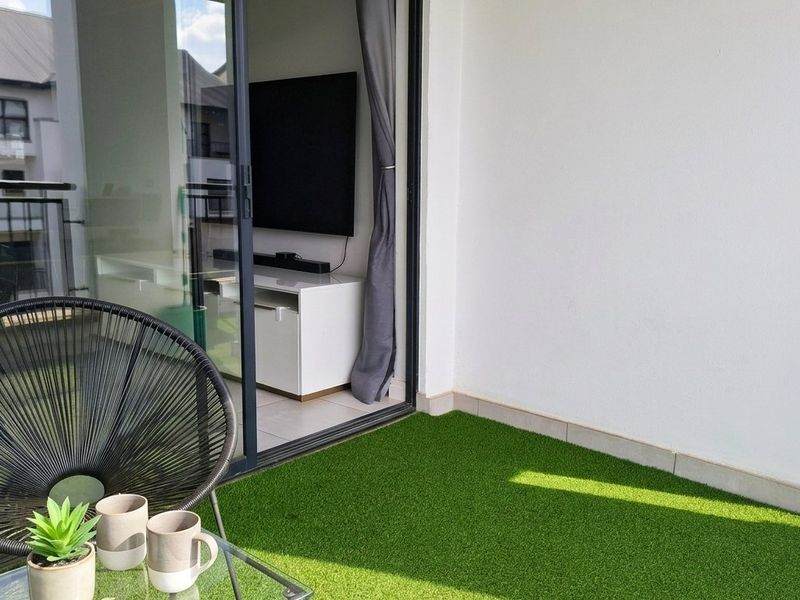A compact balcony featuring artificial turf flooring and a large sliding glass door providing seamless access to the interior living space.