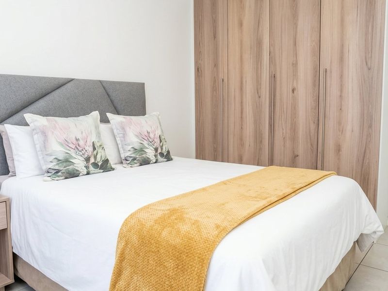 A well-maintained bedroom featuring neutral tiled flooring and modern, full-height built-in wooden cupboards providing ample storage space.