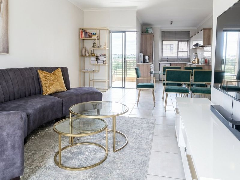 An open-plan living and dining area featuring tiled floors, a modern kitchen with built-in cabinetry, and a sliding door leading to a balcony.