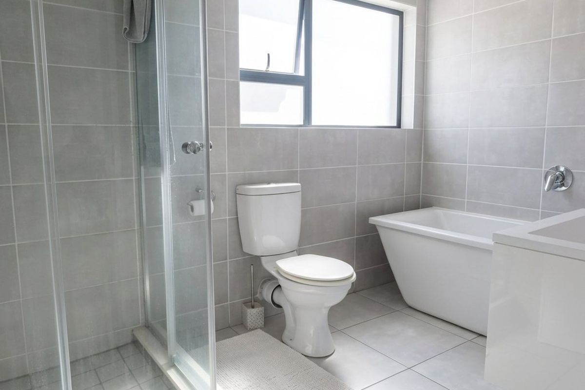 Modern bathroom featuring a glass shower enclosure, a sleek freestanding bathtub, a toilet, and a vanity with neutral grey wall and floor tiling.
