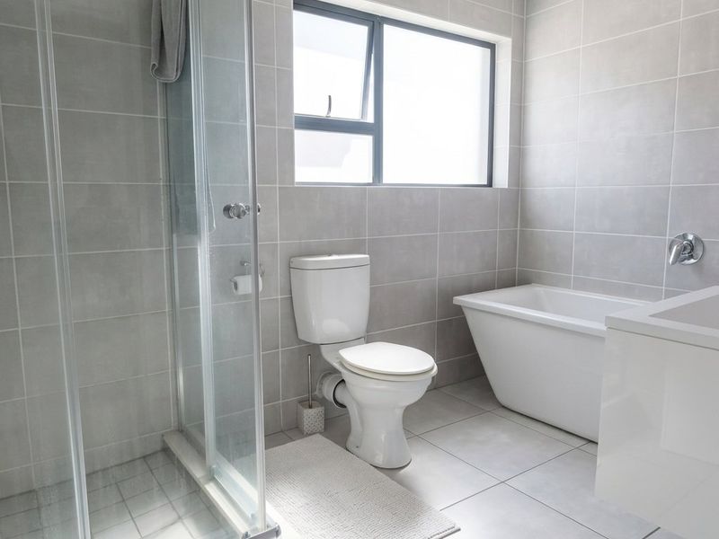 Modern bathroom featuring a glass shower enclosure, a sleek freestanding bathtub, a toilet, and a vanity with neutral grey wall and floor tiling.