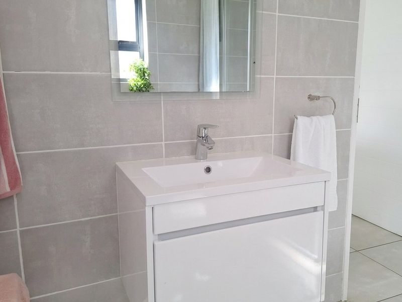A modern, well-maintained bathroom featuring a sleek wall-mounted vanity, chrome fixtures, and neutral grey wall and floor tiling.