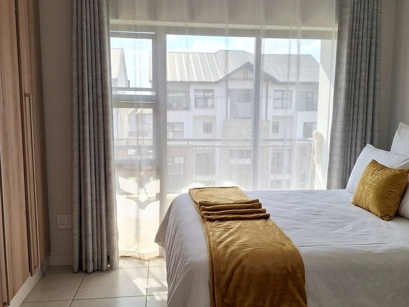 A bright bedroom featuring neutral tiled flooring, built-in cupboards, and a large sliding glass door providing natural light and access to a balcony.