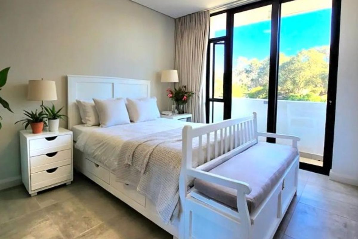 A bright bedroom featuring large sliding glass doors that open to a balcony, providing ample natural light and tiled flooring throughout.