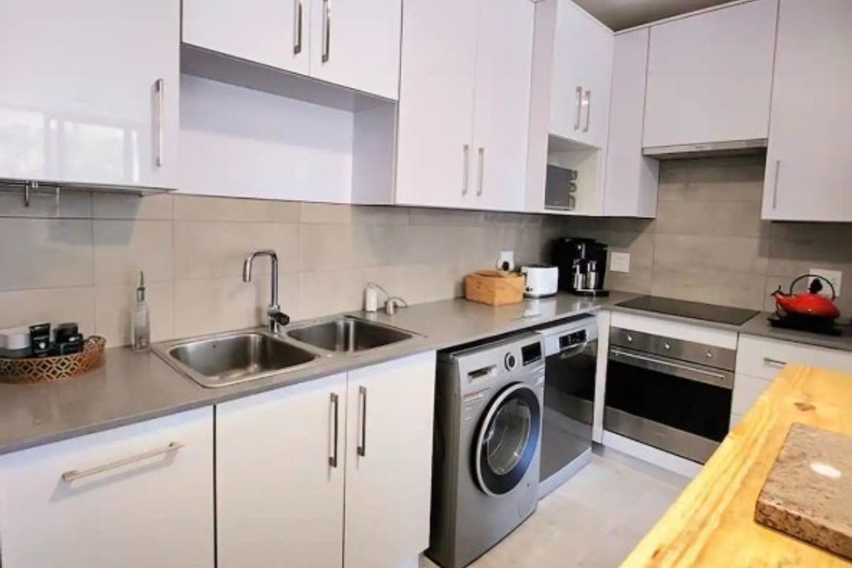 Modern kitchen featuring white high-gloss cabinetry, stone countertops, integrated appliances, and a functional layout with a built-in oven and hob.