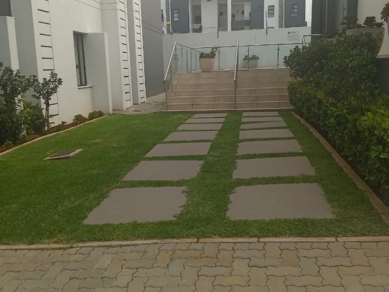 A well-maintained rear exterior area featuring a paved walkway through a lawn, leading to concrete stairs with a modern glass balustrade.