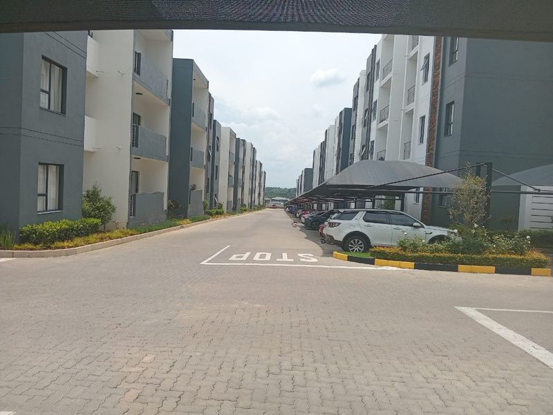 View of the apartment complex entrance featuring paved driveways, covered parking bays, and modern multi-story residential buildings.