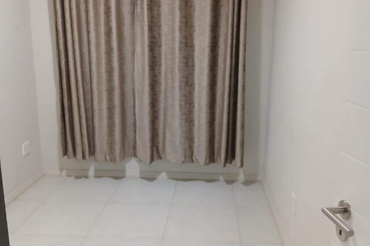 A clean, empty bedroom featuring neutral tiled flooring and a fitted curtain rod, ready for personalization.