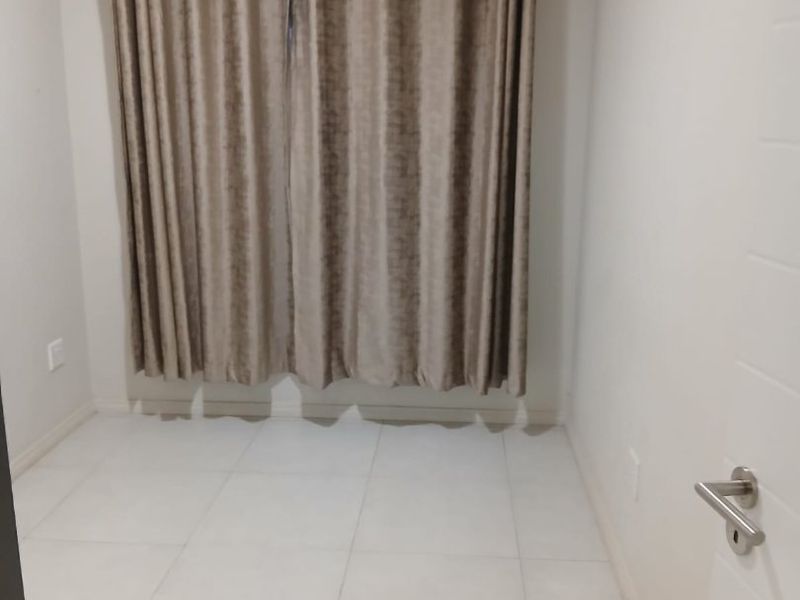 A clean, empty bedroom featuring neutral tiled flooring and a fitted curtain rod, ready for personalization.