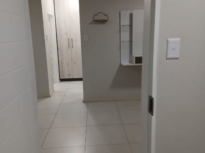 A clean and well-maintained hallway featuring neutral tiled flooring and built-in storage cupboards.