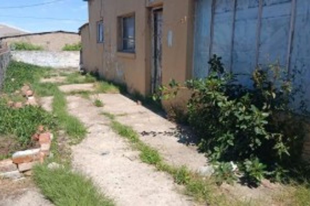 A view of the rear exterior area showing a concrete pathway, boundary wall, and signs of significant wear and maintenance requirements.