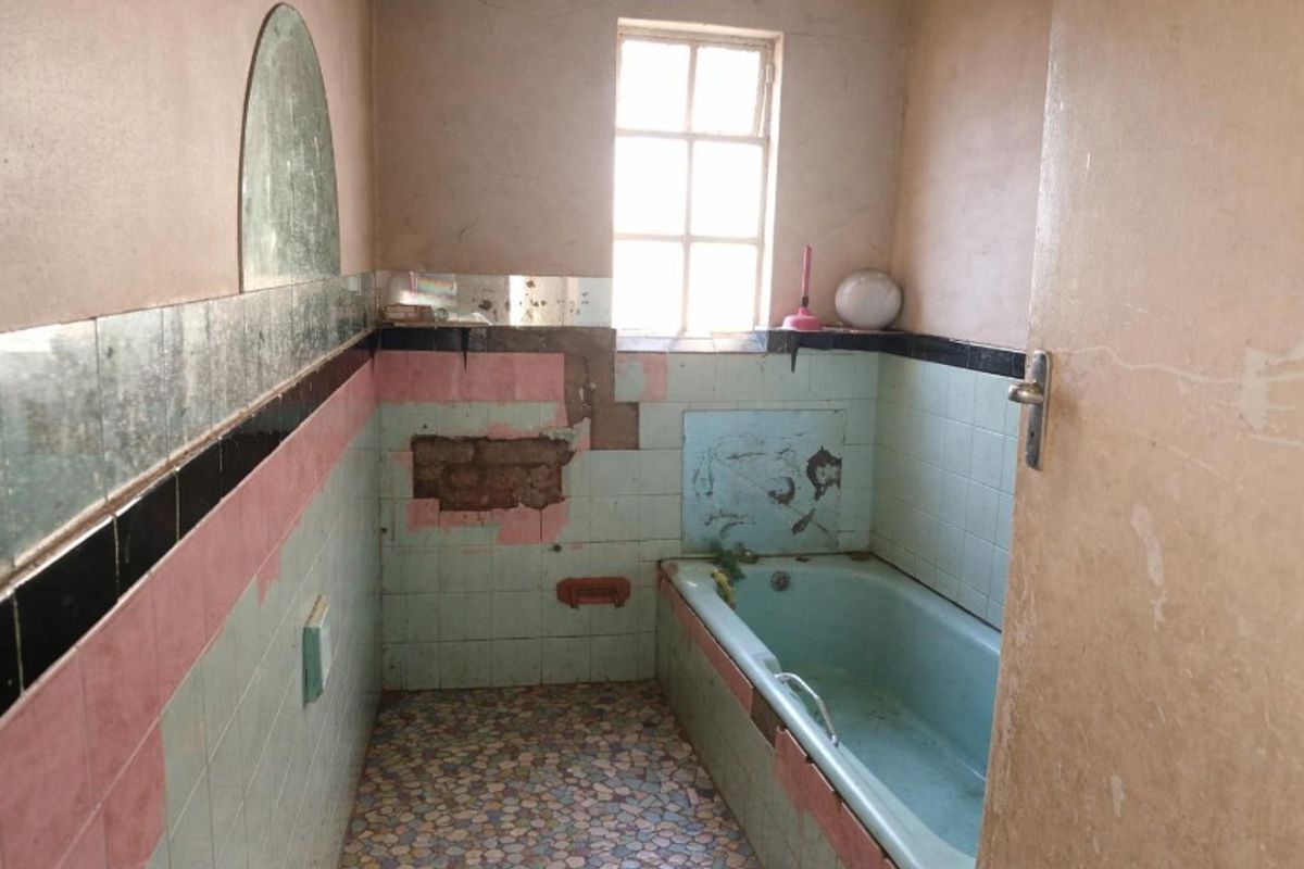 A dated bathroom featuring a built-in bathtub and original tiling, currently requiring significant renovation and repair to restore its functionality and aesthetic appeal.