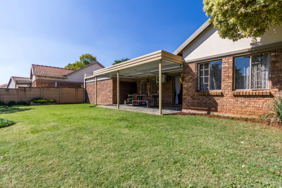 A rear view of the townhouse featuring a spacious lawn, a covered patio area, and classic brick exterior finishes.