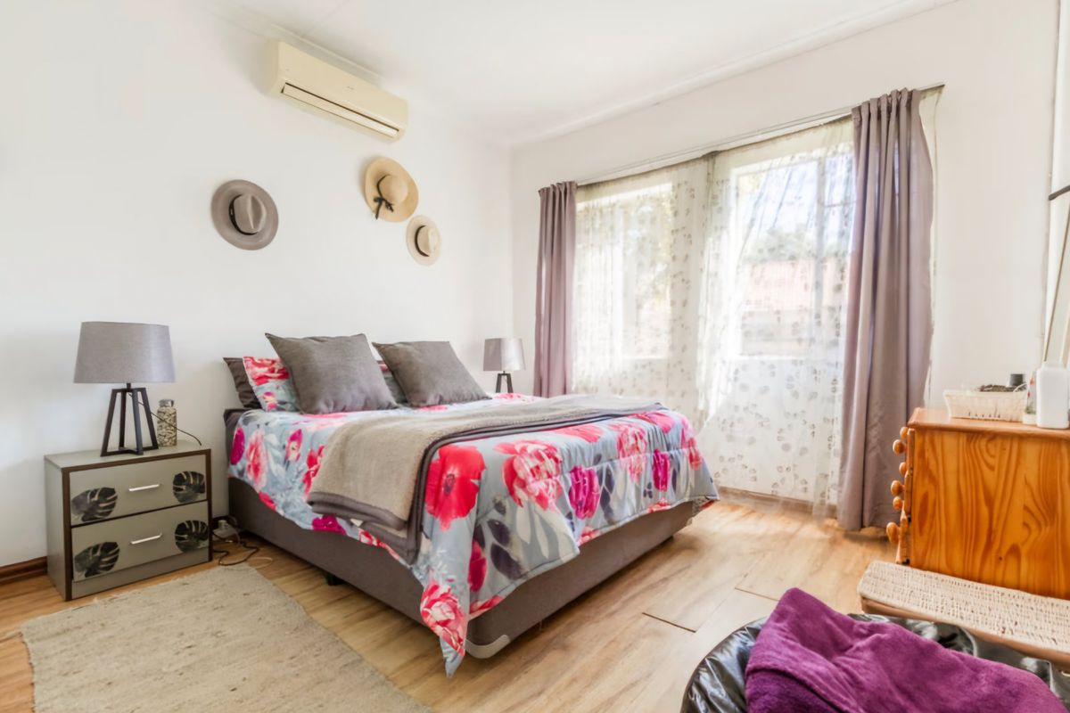 A well-lit bedroom featuring laminate flooring and a wall-mounted split-system air conditioning unit.