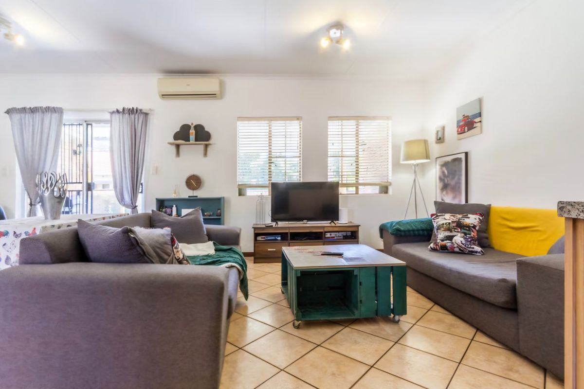 A comfortable living room featuring tiled flooring, a wall-mounted air conditioning unit, and natural light through sliding glass doors and windows.