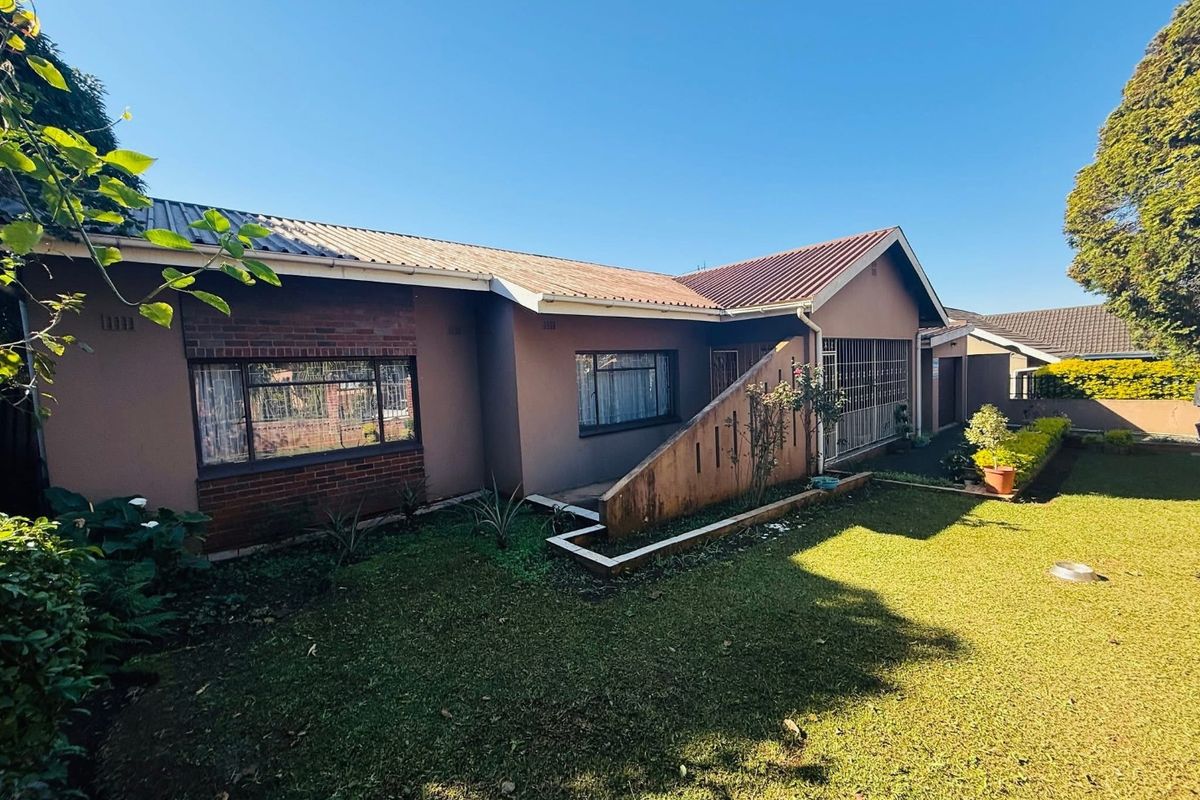 Rear view of the house featuring a brick and plaster facade, tiled roof, security bars on windows, and a landscaped garden area.