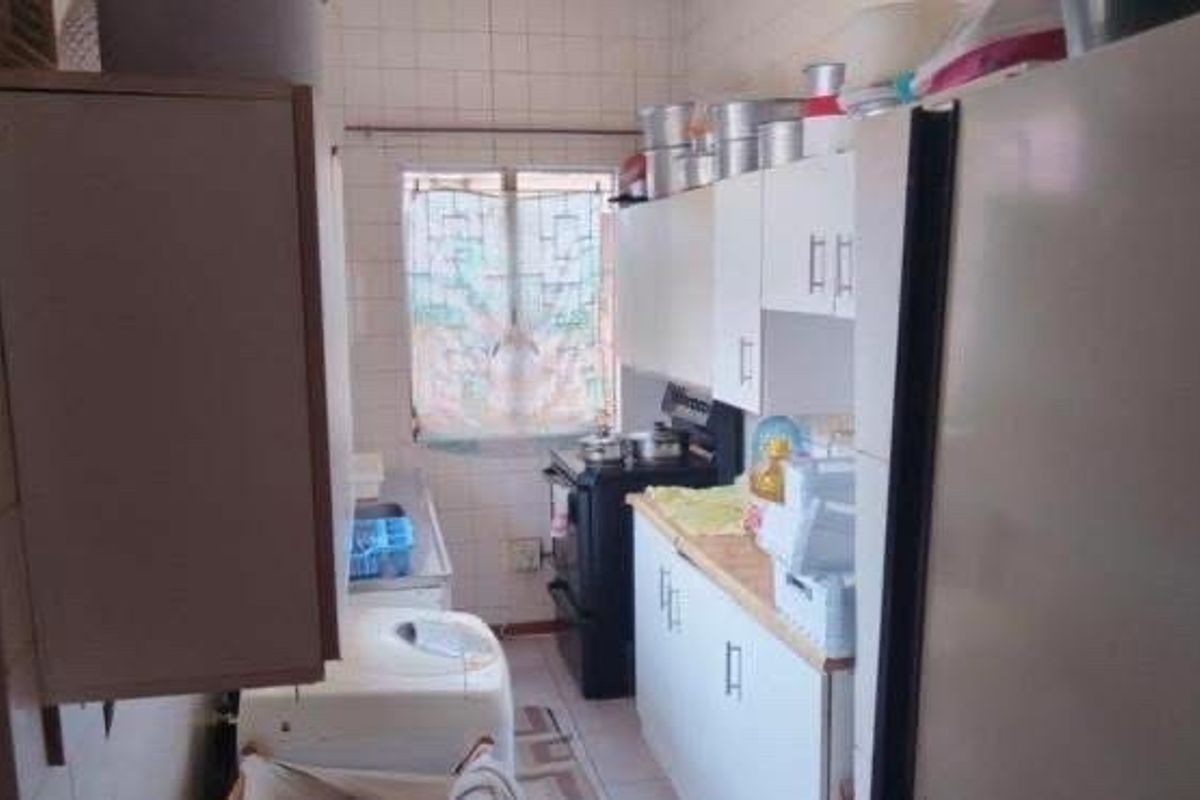 A compact kitchen featuring white built-in cabinetry, tiled walls, and a freestanding stove, offering a functional layout in need of cosmetic updates.