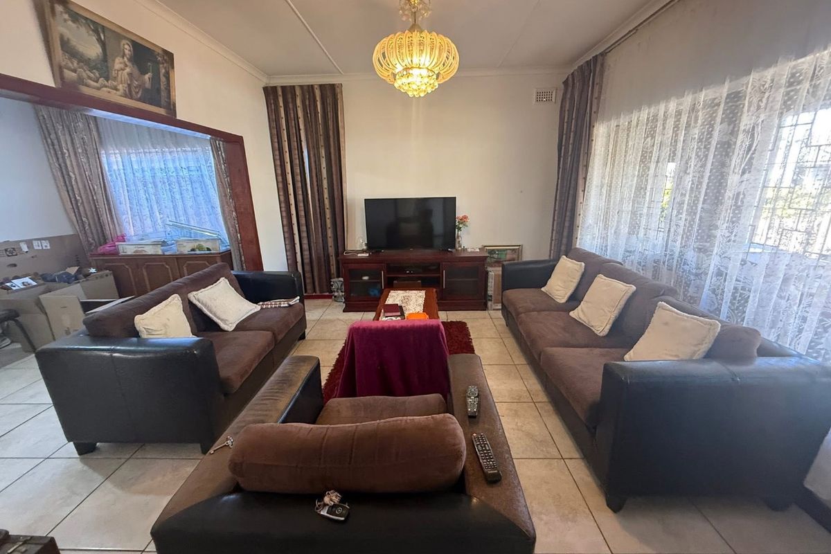 A spacious living room featuring tiled flooring, a decorative chandelier, and large windows with security bars, offering a functional and well-lit living space.