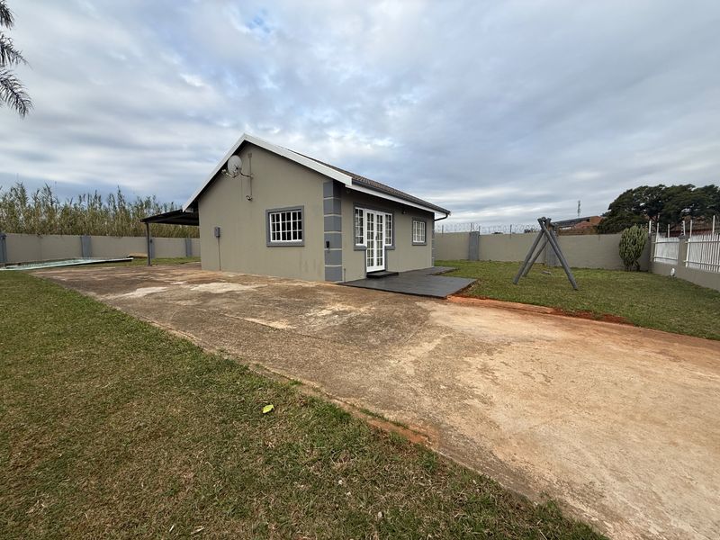 Rear view of the property featuring a large concrete driveway, a swimming pool, and a patio area enclosed by a perimeter wall with electric fencing.